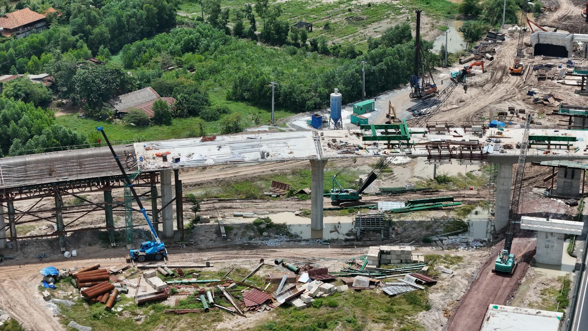 Aerial shot showing the construction of a bridge in a rural area of Vietnam, highlighting the progress and machinery involved.